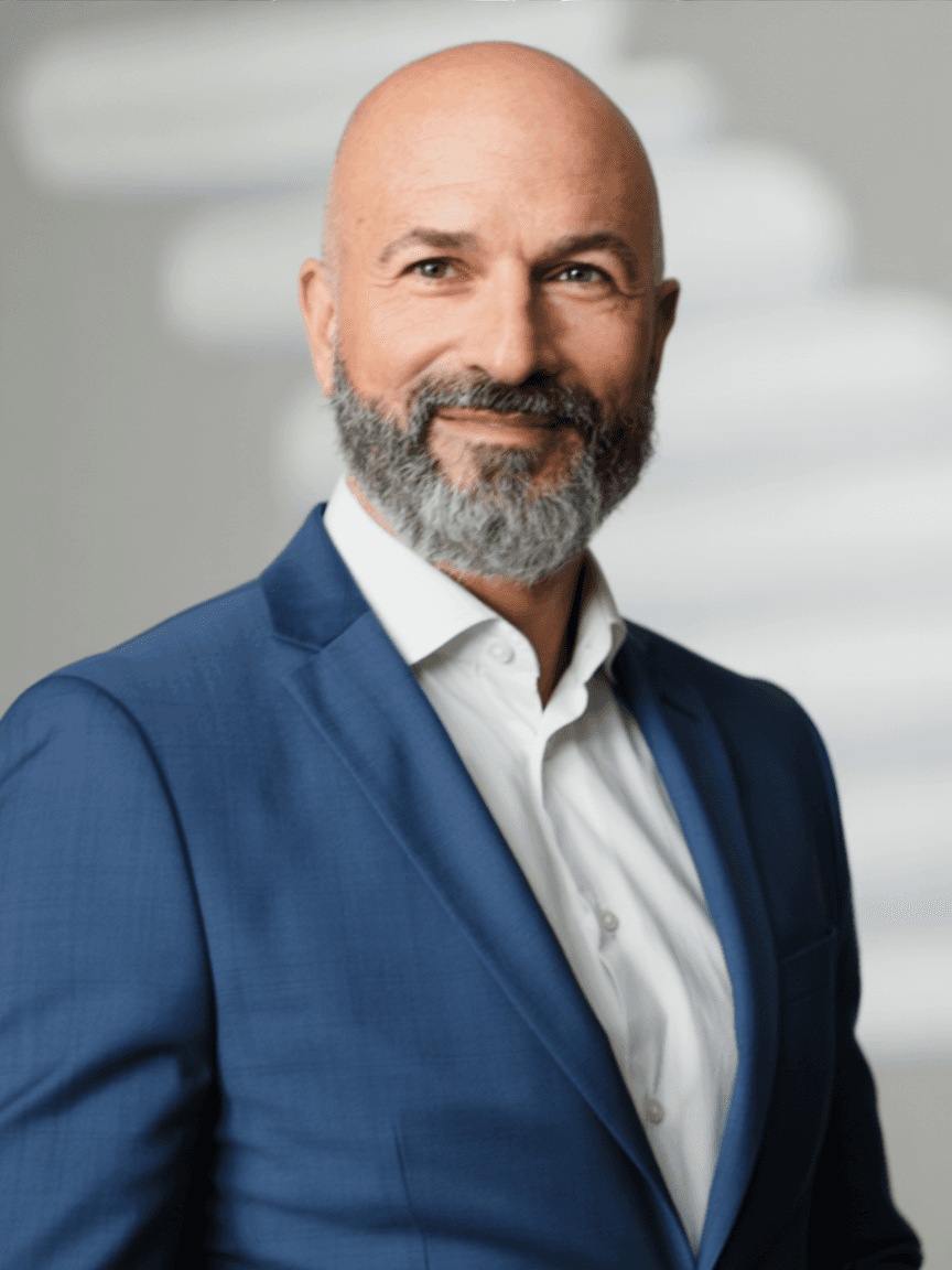 Smiling bald man with a salt-and-pepper beard wearing a blue blazer and white shirt.